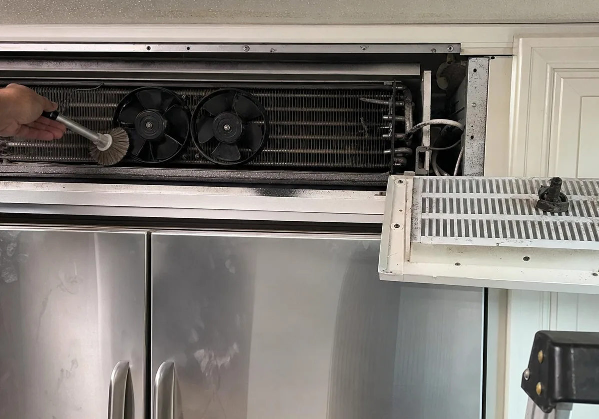 Twin condenser fans and a cleaned coil behind an opened refrigerator grille panel